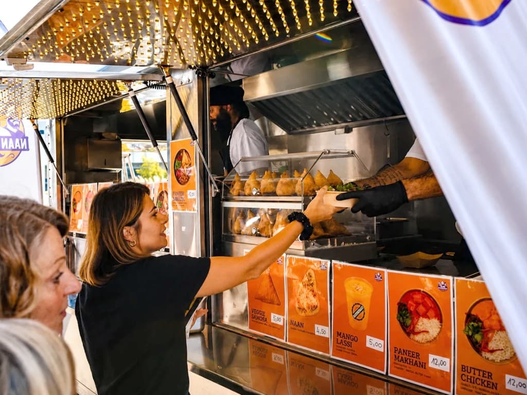 Ausgabe am Naan Brüder Foodtruck – eine Gästin nimmt eine Bowl entgegen